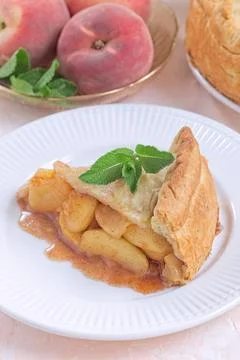 Old fashioned deep dish peach pie slice garnished with fresh mint, on white Foto stock