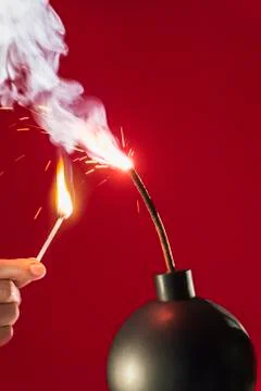 Old-fashioned explosive device ready to go off with hand holding burning match Stock Photos