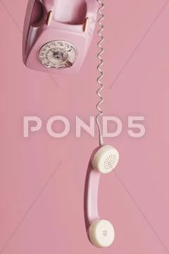 Old Fashioned Pink Dial Telephone With Hanging Receiver Against Pink Background