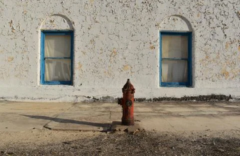 Old fire hydrant on the background of a white wall and blue windows Stock Photos