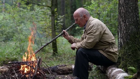 Old forester is lighting fire in forest, hiking and resting in nature 動画素材 167006905
