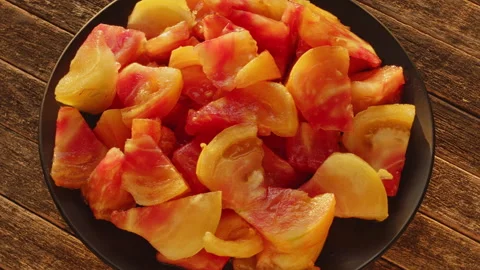 Old German tomato wedges rotating on black plate top view. Stock Footage 343891785