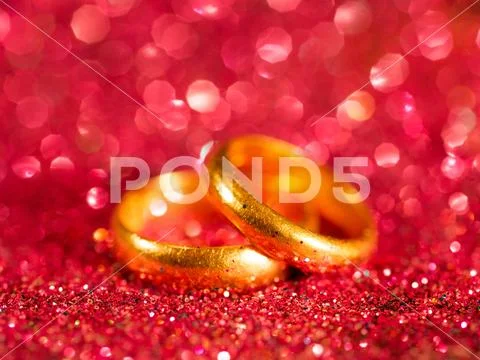 Old golden wedding rings on blurred red sparkle background Stock Photos