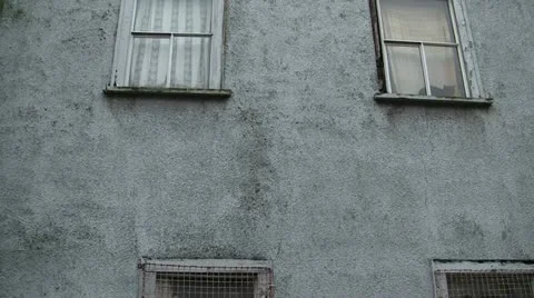 Old Gray Building Grated Windows Pan Down To Mossy Base Stock Footage 16247942
