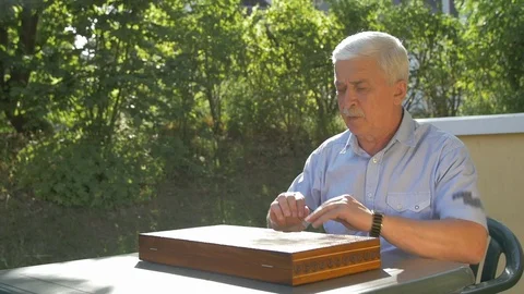 Old gray-haired man opens the chess game outside in the garden at the table and Stock Footage 118462105