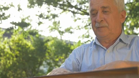 Old gray-haired man opens the chess game outside in the garden at the table and Stock Footage 118699664
