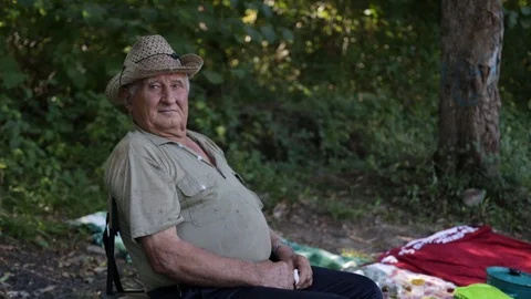 An old gray-haired man with a pensive face, in a straw hat sits on a chair in th Stock Footage 120166119