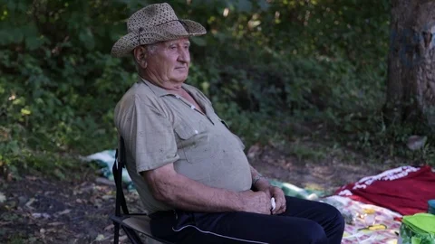 An old gray-haired man with a pensive face, in a straw hat sits on a chair in th Stock Footage 120166121