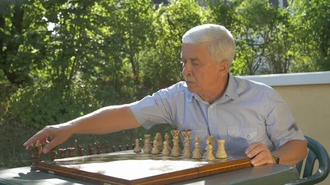 Old gray-haired man prepares the chess game outside in the garden at the table Stock Footage 118534174
