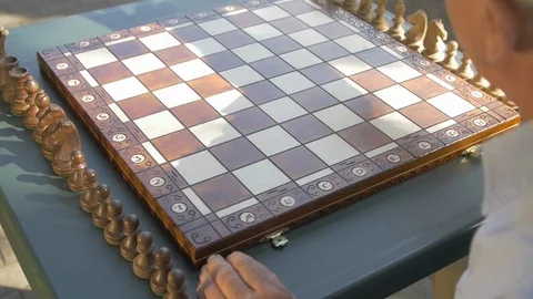 Old gray-haired man prepares the chess game outside in the garden at the table Stock Footage 118608816
