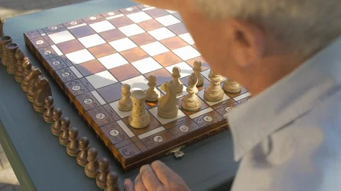 Old gray-haired man prepares the chess game outside in the garden at the table Stock Footage 118612282