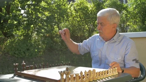 Old gray-haired man repares the chess game outside in the garden at the table Stock Footage 118465588