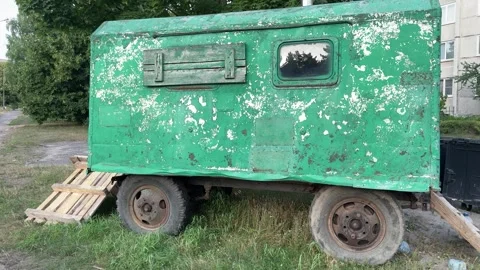 Old green trailer with peeling paint and rusty wheels parked on grass Stock Footage 341830091