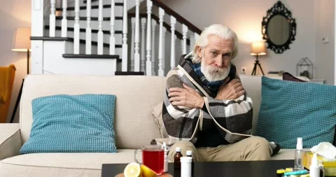 Old grey-haired bearded sick man in warm plaid sitting on sofa indoors and Stock Footage 141322274