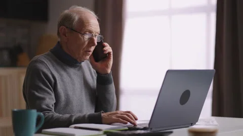 Old grey haired man is working at home office, accountant is calling by cell Stock Footage 153531482