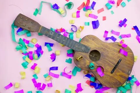 Old guitar with torn strings in multi-colored confetti on a pink background Foto stock
