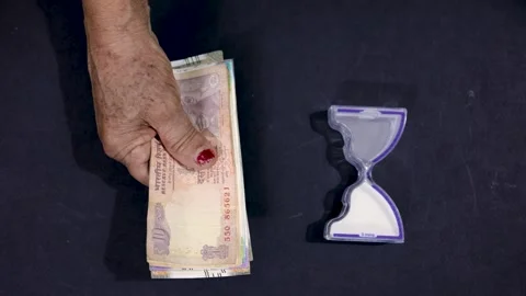 Old hand holding Indian banknotes with Sand Timer symbolizing monetary inde.. Stock Footage 318357377