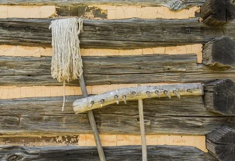 Old hand made farming tools of wooden rake and string mop leaning against log Stock Photos