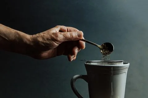A old hand preparing a tea over a dark background with copy space and dark .. Stock Photos
