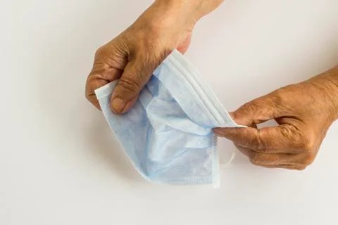 Old hands holding of single use hygenic face mask on white background Stock Photos