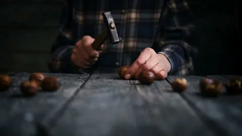Old hands of a man holding a hammer and breaking walnuts on a wooden table. Stock Footage 86449947