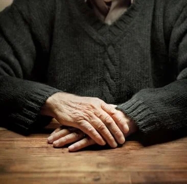 Old hands on a wooden table with dramatic lighting Stock Photos