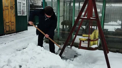 An old handsome man cleans snow in the courtyard of a private house. Stock Footage 169608574
