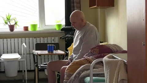An old helpless man sits on a bed in a hospice, a shelter for the elderly. Stock-Footage 307167541