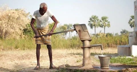 Old Indian man pushing handpump to fill bucket with water during daytime. Stock Footage 296327026