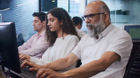 Old Indian man sitting in front of computer with office colleagues busy working Stock Footage 196982208