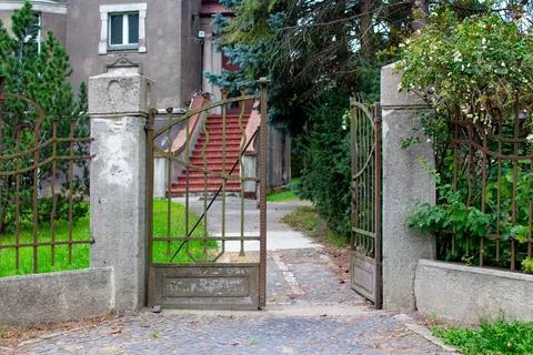 Old iron gate opens to a quiet pathway leading to an vintage house Stock Photos