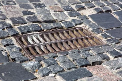 The old iron grate of the drainage system hatch on the road paved. Stock Photos