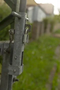 Old iron lock securing gate amidst soft green bokeh and distant home outlines Stock Photos