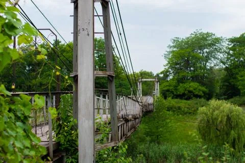 Old iron non-functioning suspension bridge over a dried river side view. Stock Photos