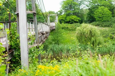 Old iron non-functioning suspension bridge over a dried river side view. Bright Stock Photos