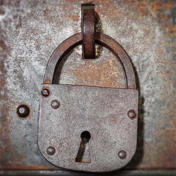 Old iron padlock hangs on a weathered metal door with rivets and rust, evok.. Stock Photos
