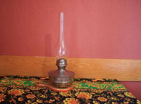 An old kerosene lamp on a kitchen table covered with a beautiful tablecloth Stock Photos