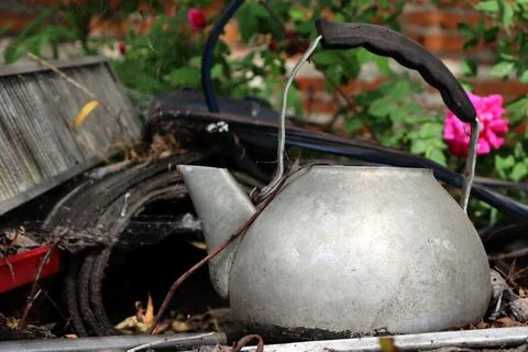 Old kettle rests on forgotten items in a garden with flowers in the background Foto stock