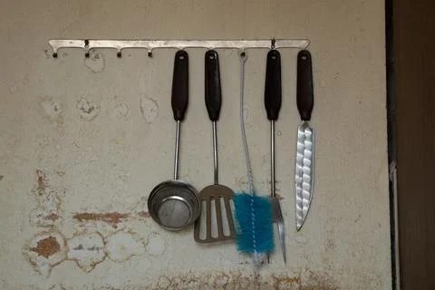 Old kitchen utensils such as a sieve, spatula, brush, knife hang on metal hoo Stock Photos