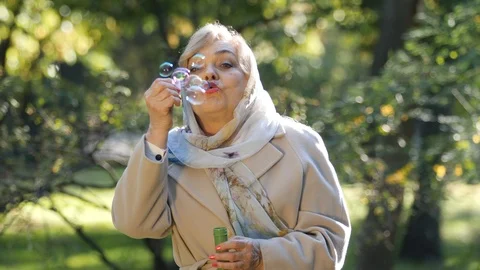 Old lady blows soap bubbles out in park. 스톡 동영상 118236398