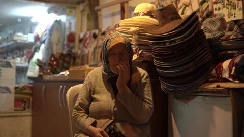 Old lady in brown warm sweater sits on chair selling hats Stock Footage 149576552