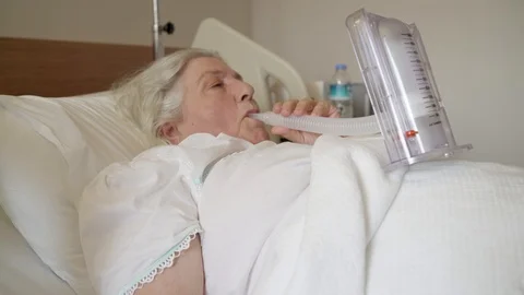 An old lady is doing a breathing exercise by inhaling a medical tool. Stock Footage 106886191