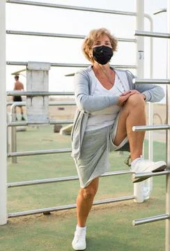 Old lady in face mask doing exercises outdoors Stock Photos