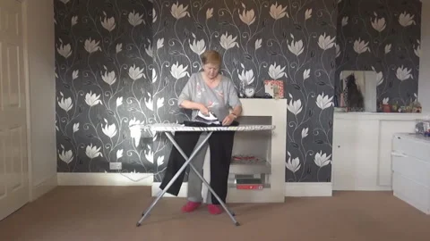 An old lady irons clothes whilst dancing Stock Footage 86478045