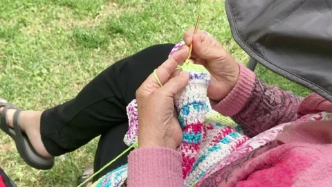 Old lady knits yarn wool with knitting needles while sitting outdoor - 4K Stock Footage 198770323