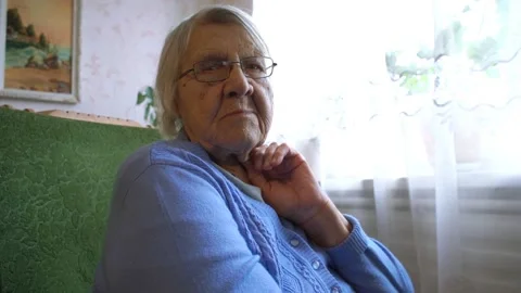 Old lady looking at camera while sitting in a cozy chair next to the window Stock Footage 134022501