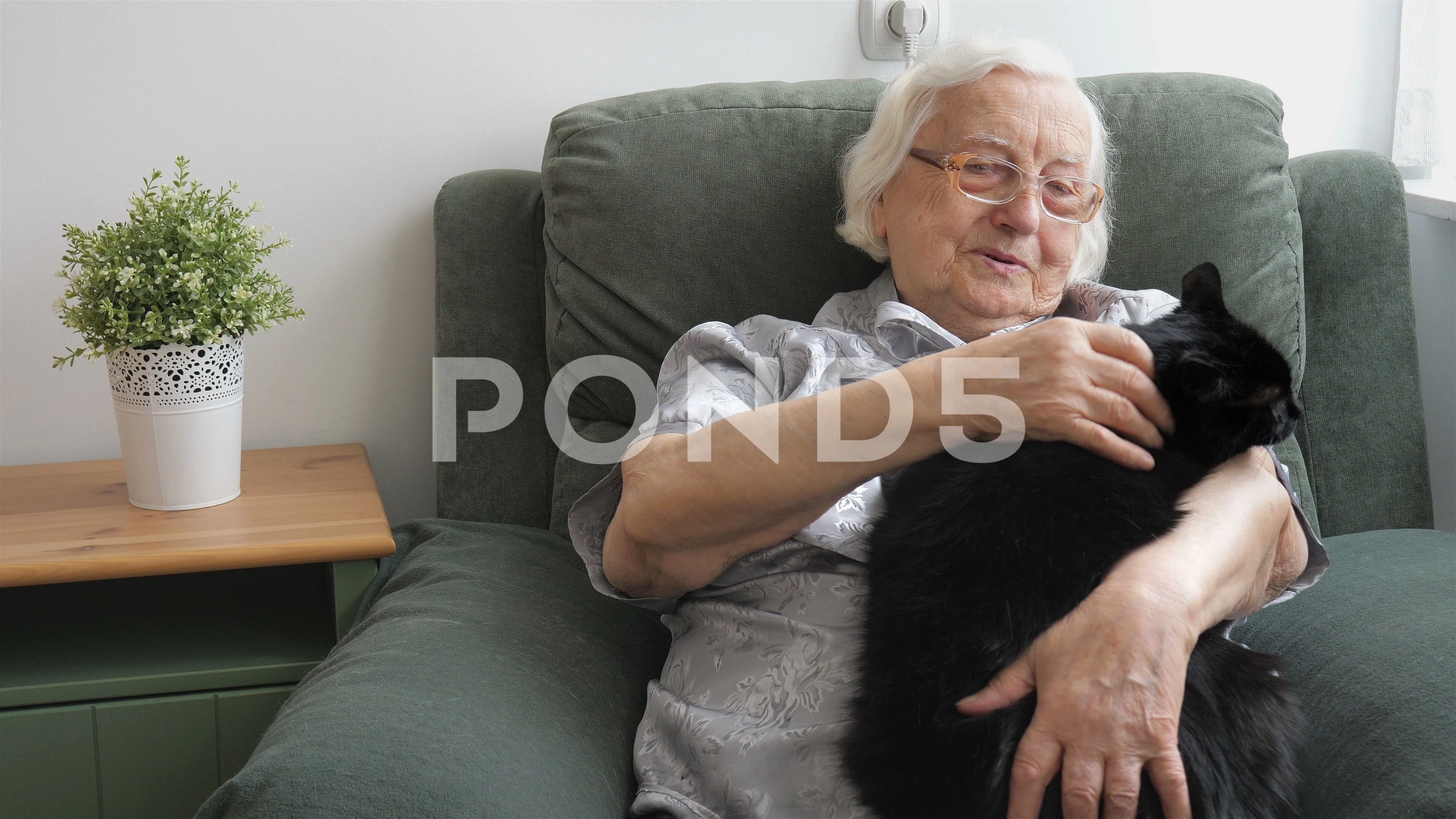 An old lady is petting a black, fat cat