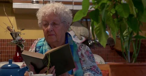 Old lady reading a book in the kitchen Stock Footage 81358501