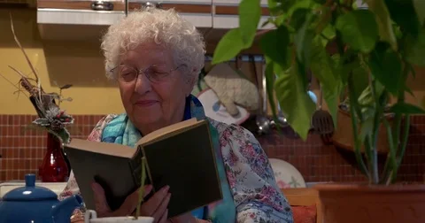 Old lady reading a book smiling in the kitchen Stock Footage