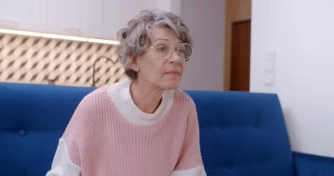 Old lady sits on a couch and turns on TV , 4k Stock Footage 231920701